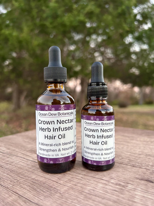 Two bottles of Crown Nectar Herb Infused Hair Oil on a wooden surface with a blurred natural background.