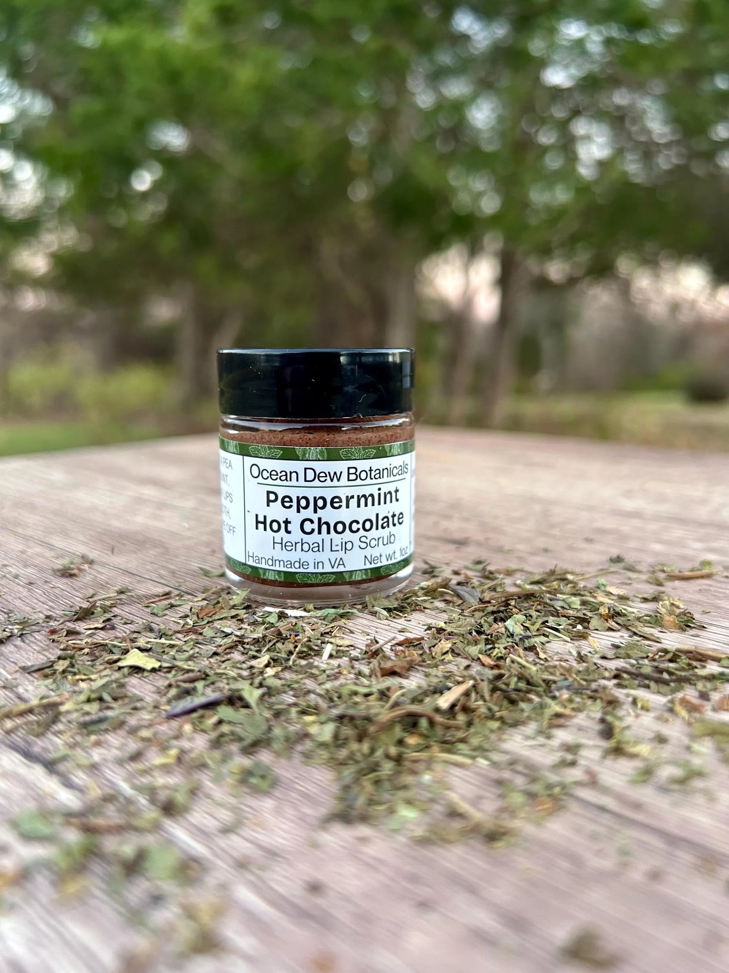 Peppermint hot chocolate herbal lip scrub jar on a wooden surface with dried herbs.